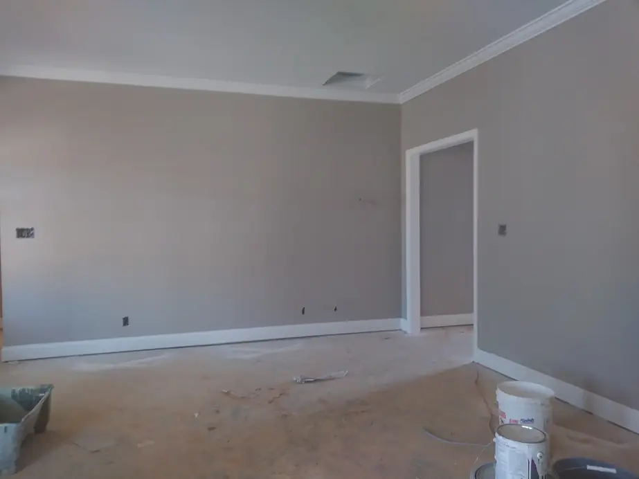 Greige living room walls with white crown moulding, roller tray and paint cans on the floor